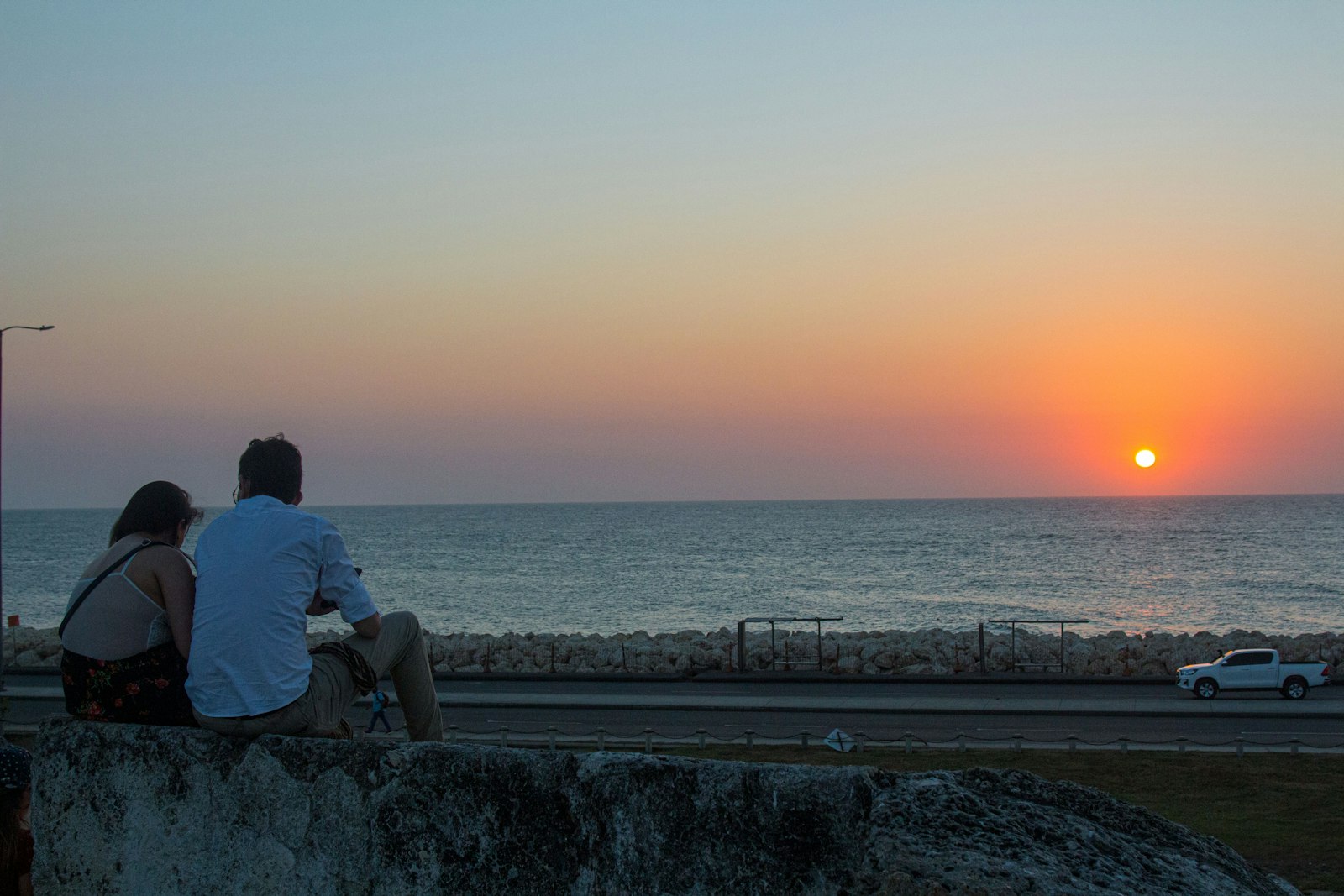 Pareja sentada sobre la muralla de Cartagena mirando el atardecer